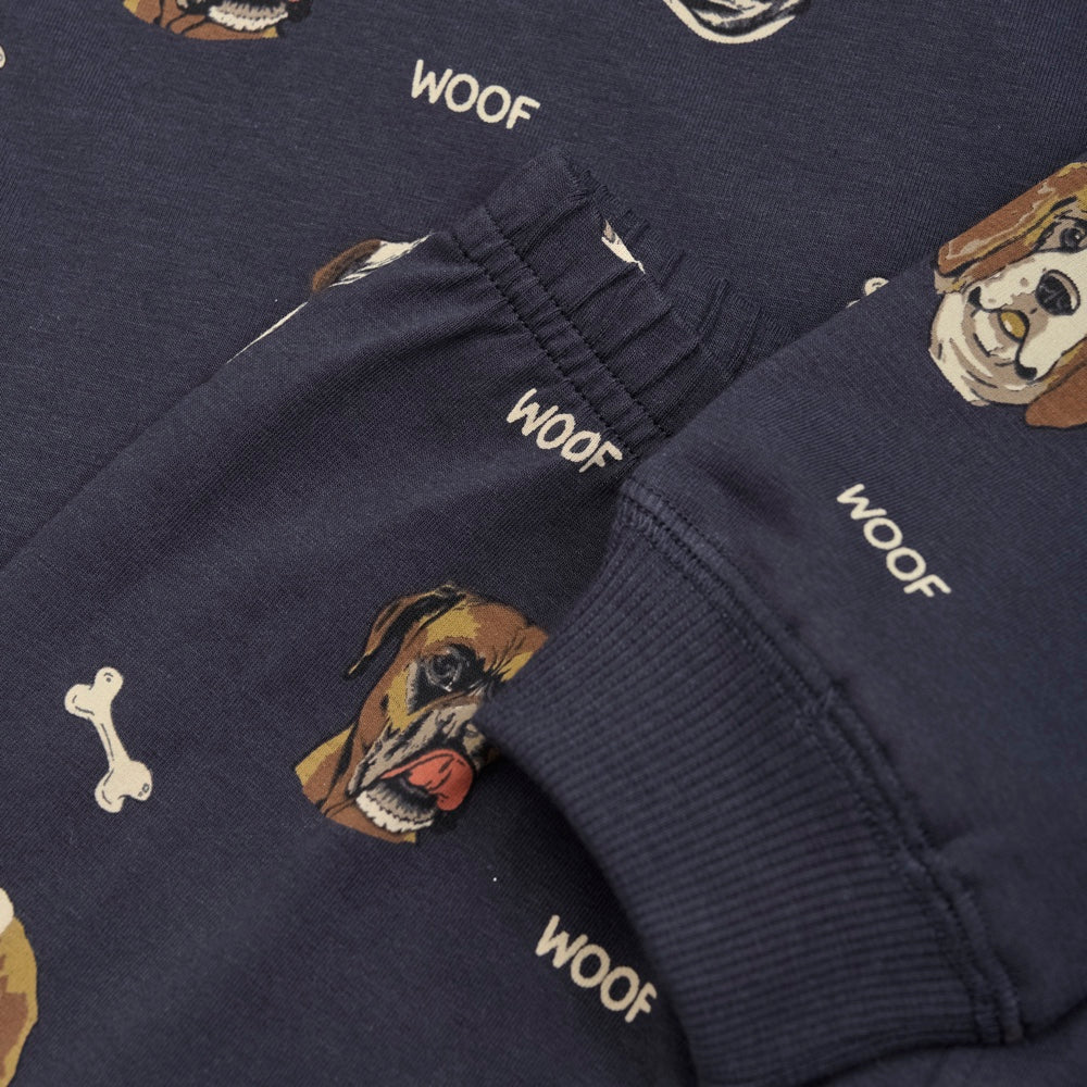 Nahaufnahme Ärmel und Bund
Der Pyjama besteht aus einem langärmeligen T-Shirt und einer Hose. Der Pyjama ist aus einer weichen Baumwollmischung gefertigt und hat einen Allover-Hundedruck. Die Hose hat einen Gummizug an der Taille, der für eine gute und bequeme Passform sorgt. Gerippte Kanten an Hals, Handgelenken und Knöcheln. 