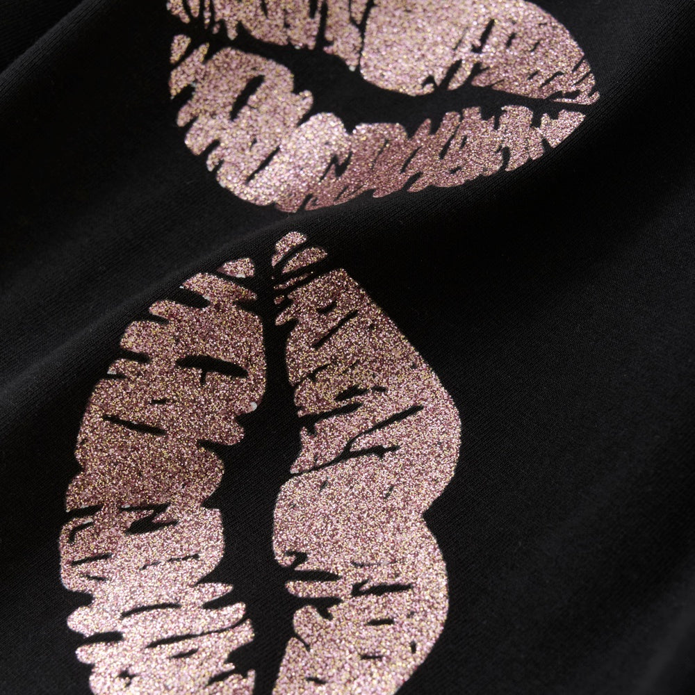 Schlichtes Langarmshirt mit glitzerndem Lippenprint. Die Bluse hat einen Rundhalsausschnitt und einen leichten Falteneffekt an den Schultern. Es besteht aus weicher Baumwollqualität mit etwas Stretch. Nahaufnahme
