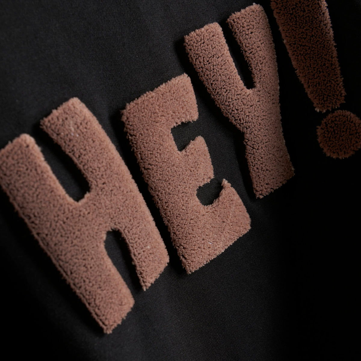 Der Pullover hat einen Schriftzug mit "Hey" in 3 D Optik aufgenäht. Er hat Bündchen an der Taille und an den Ärmeln. 